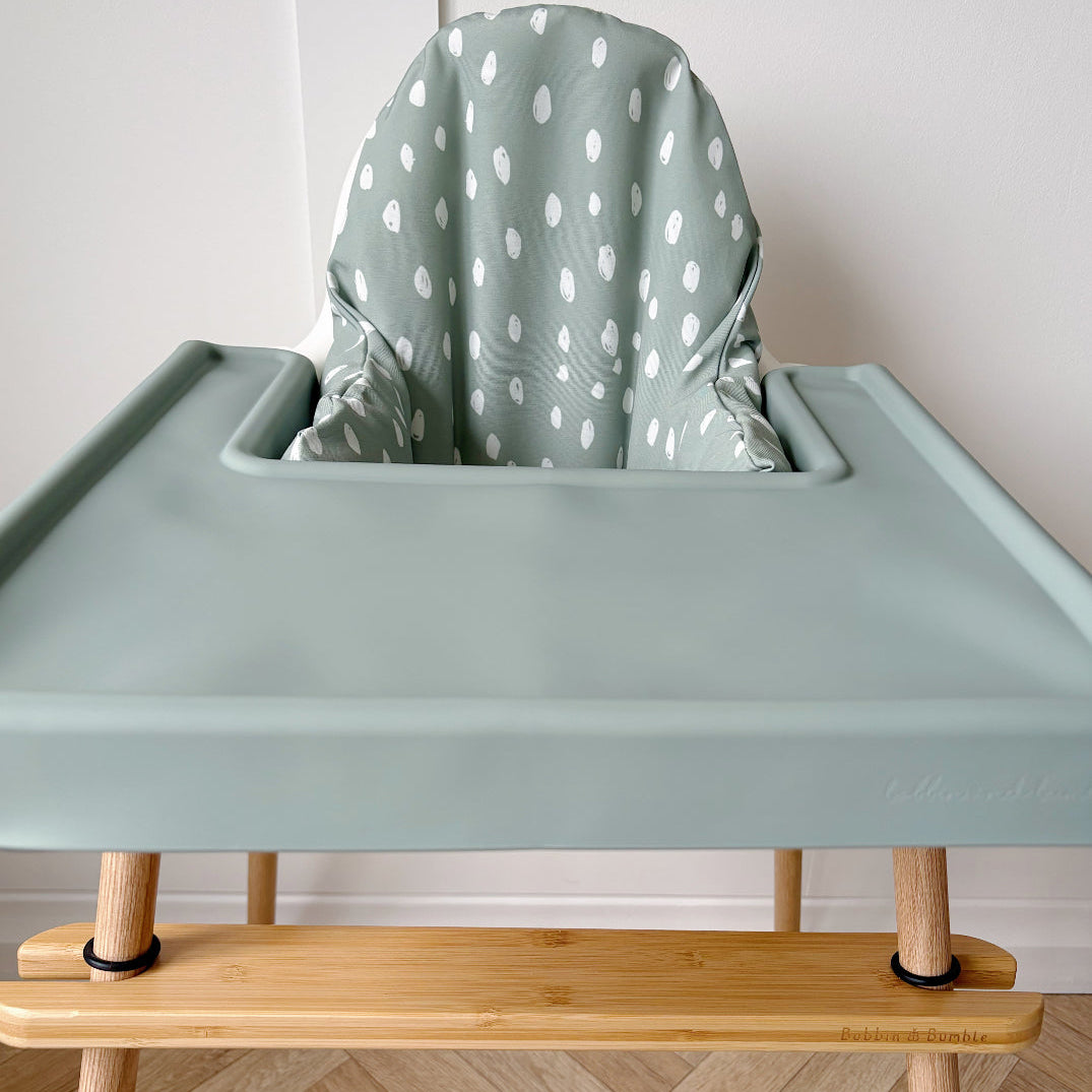 Green high chair with a polka dot cover on a wooden floor.