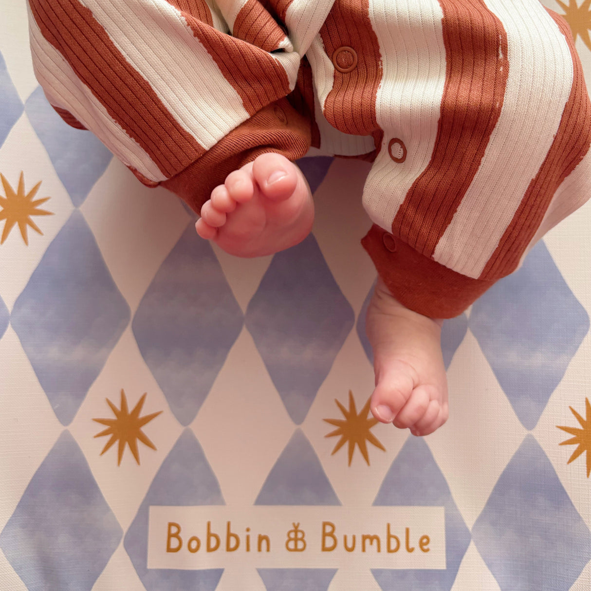 Baby's legs in striped pants on a patterned surface with 'Bobbin & Bumble' branding.