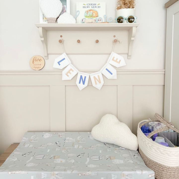 Wedge changing mat underneath a shelf which features a name flag saying lennie.