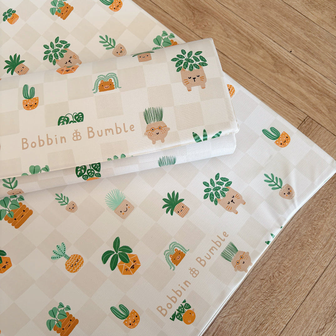 Baby changing mats with illustrated plant design and 'Bobbin & Bumble' branding on a wooden floor.