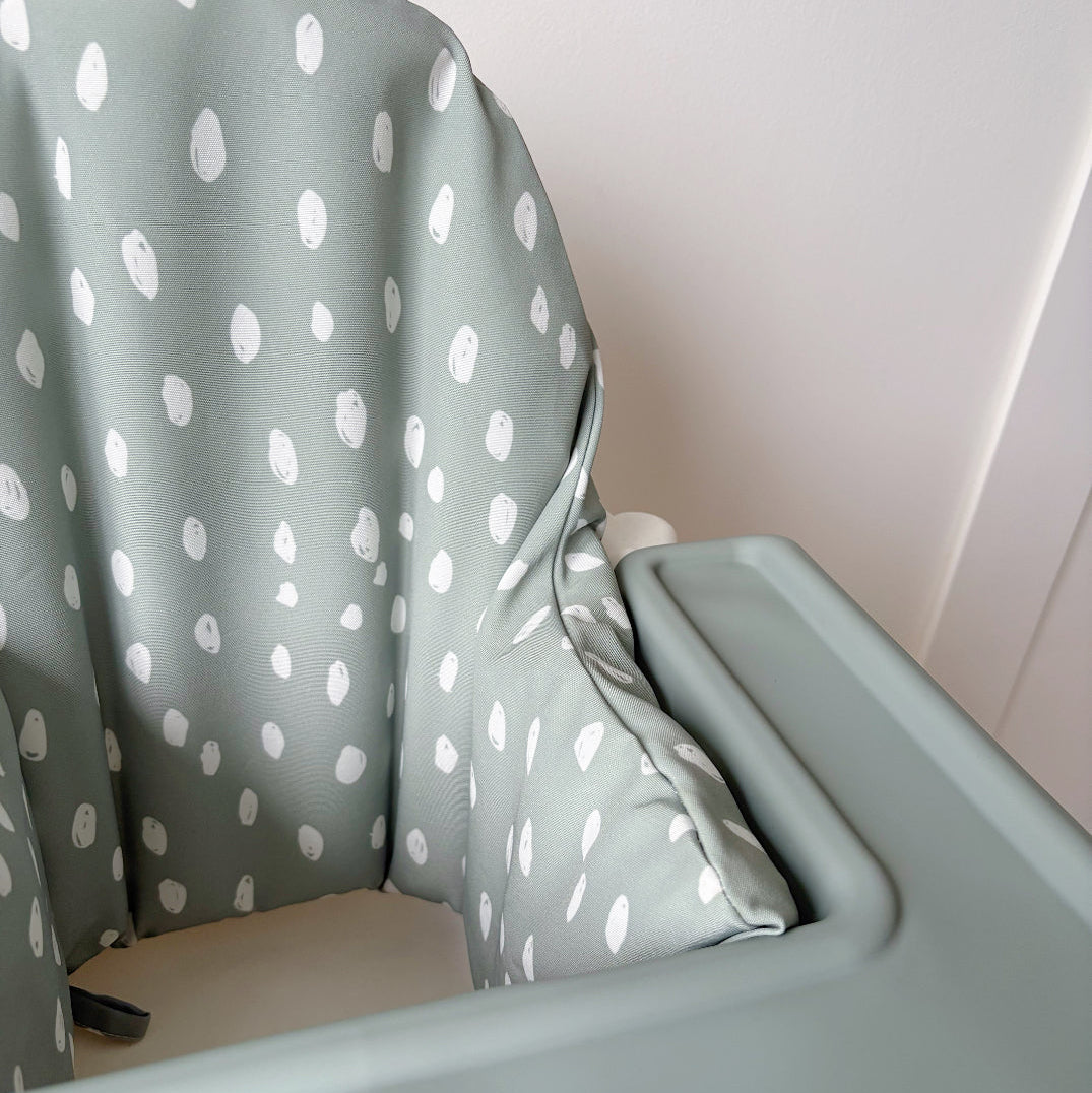 Green high chair cover with a polka dot cover against a white wall