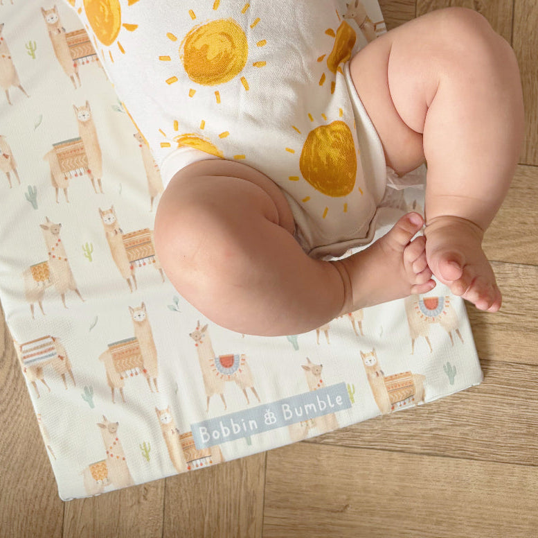 Baby laying on a colourful changing mat with alpacas on a wooden floor