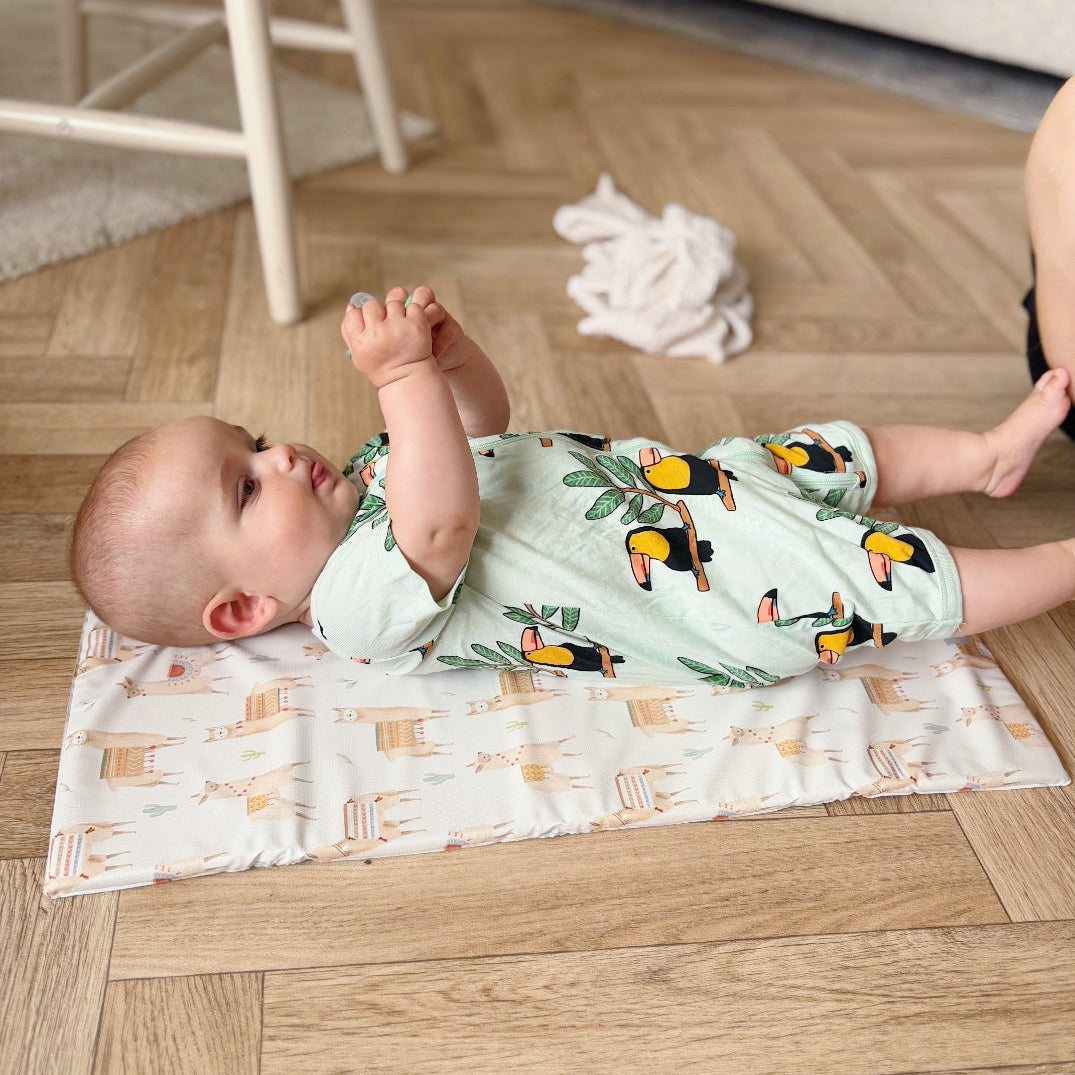 Baby lying on a mat with a toucan pattern romper on a wooden floor