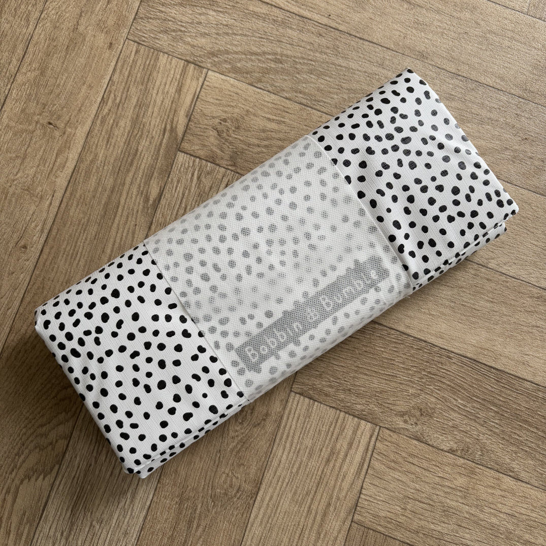Folded travel baby changing mat with black polka dots pattern on a wooden floor