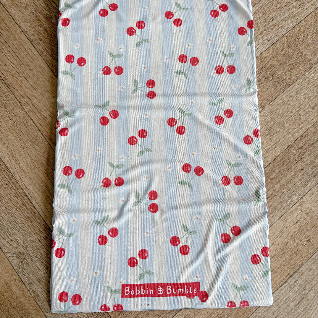 Travel changing mat laid flat with cherry pattern on a wooden surface