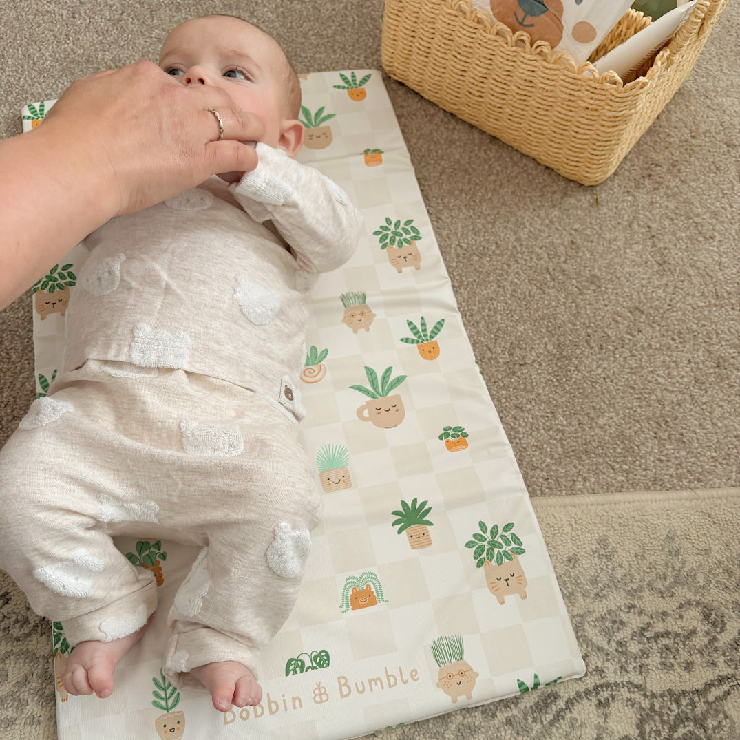 Baby laying on a patterned changing mat with a person assisting, in a home setting.