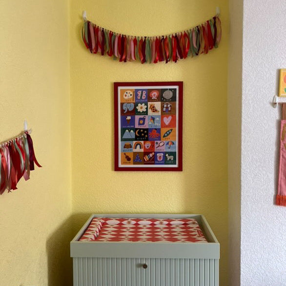 Children's room with yellow wall, colorful banner, and framed picture.