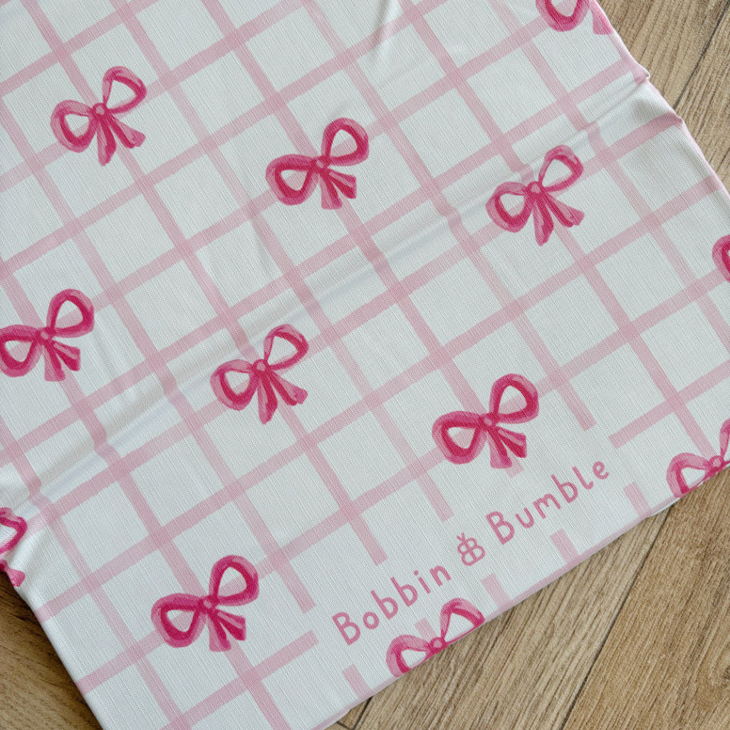 Travel baby changing mat with pink bow pattern and 'Bobbin & Bumble' branding on a wooden surface
