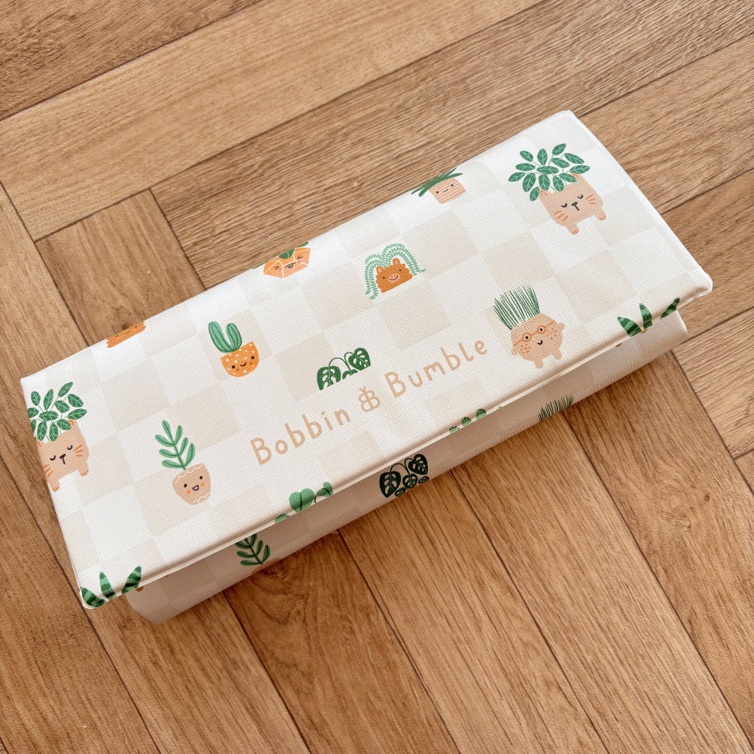 Travel baby changing mat, folded, with plant-themed wrapping on a wooden floor