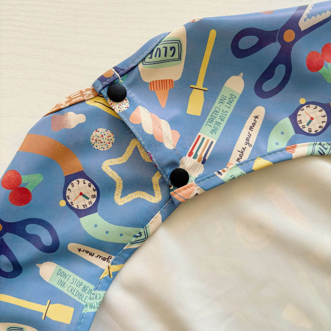 Colorful children's apron with various items on a beige background. Popper close