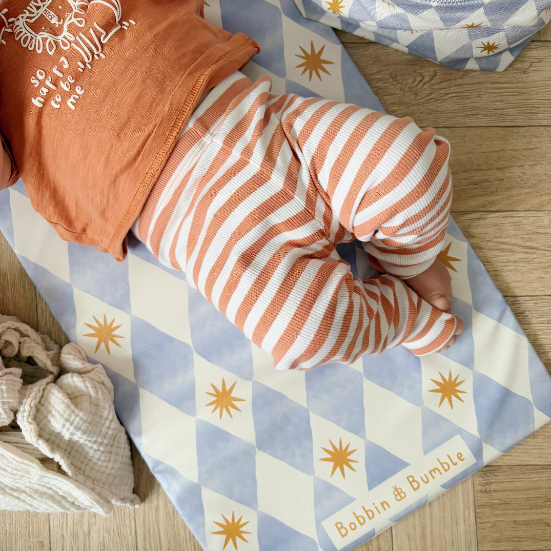 Baby in orange and white striped outfit lying on a blue and white checkered blanket with sun patterns.