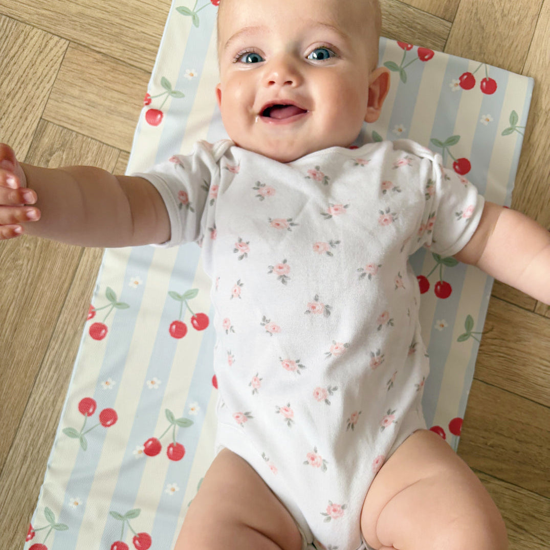 Baby in a floral onesie laying on a cherry-patterned mat with 'Bobbin & Bumble' branding.