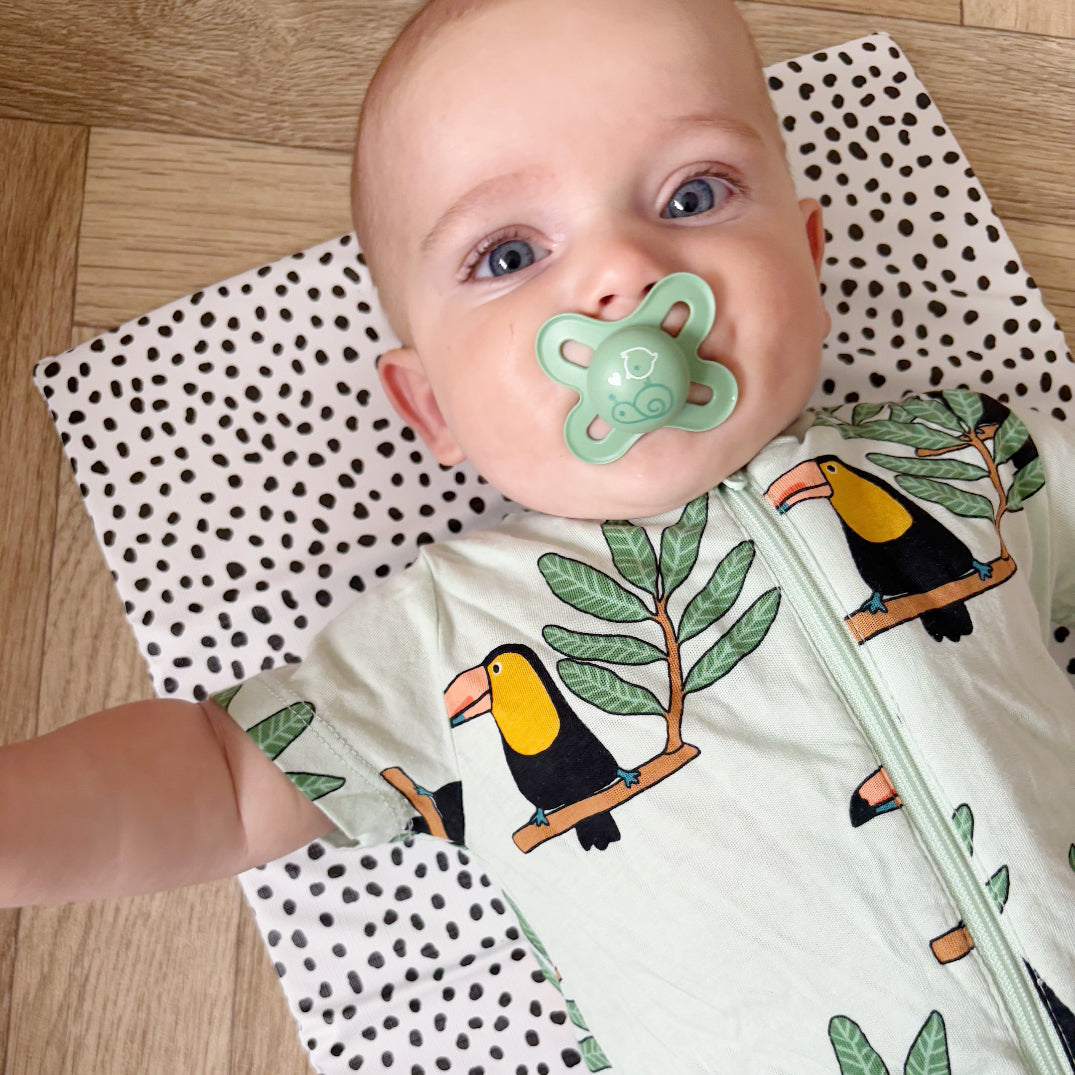 Baby wearing a onesie with toucan designs on a polka dot travel changing mat