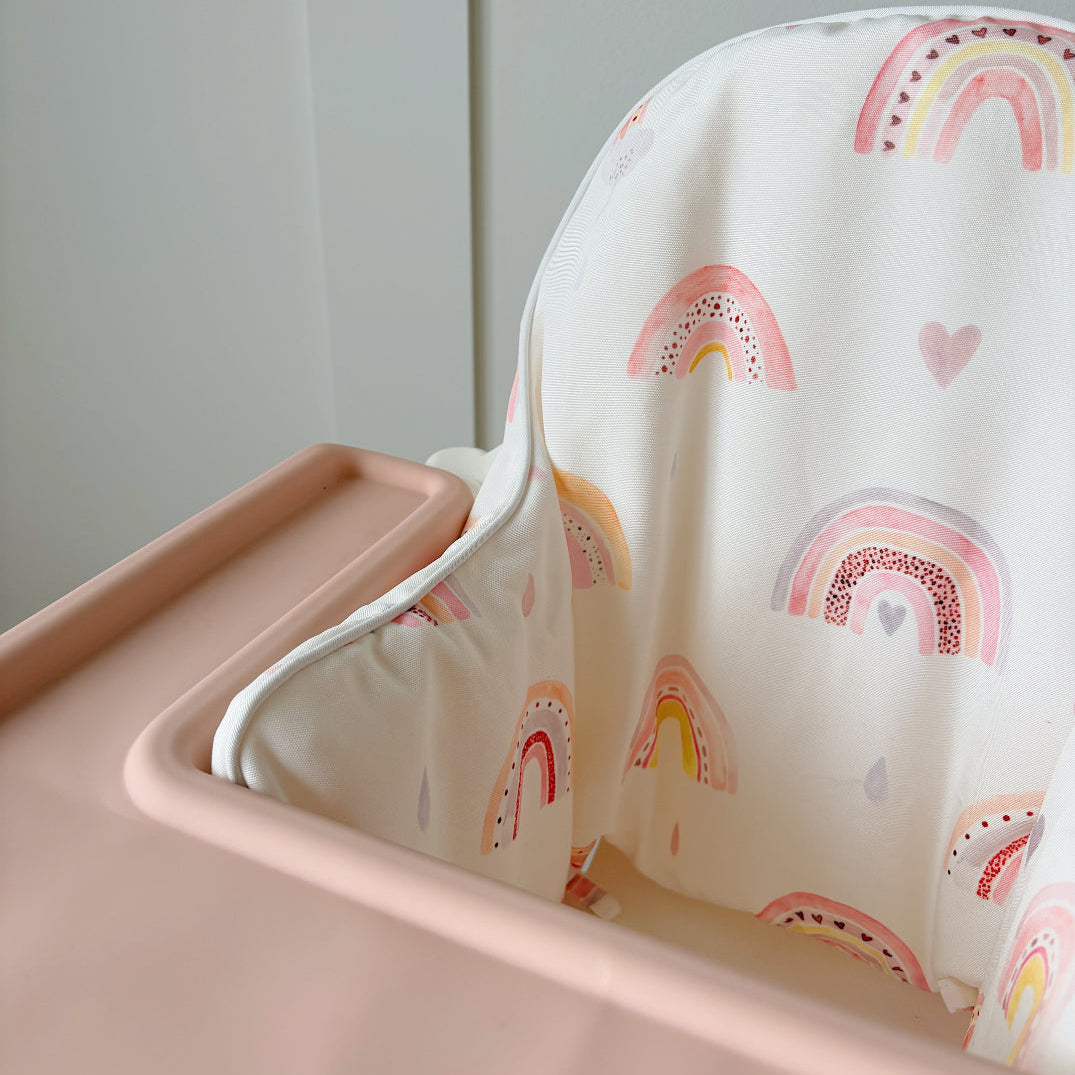 Pink high chair with a white cover featuring rainbow patterns on a light gray background
