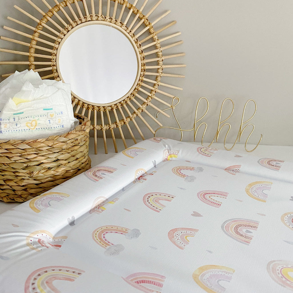 rainbow baby changing mat against a grey background with a sunburst ratten mirror and basket of nappies