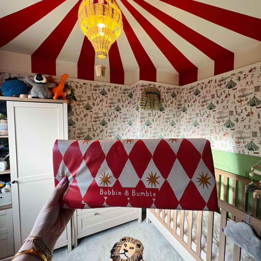 Red harlequin travel changing mat being held up in a circus themed nursery