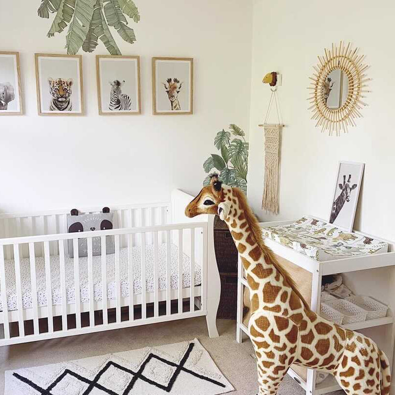 Safari themed nursery with green plants, giraffe teddy bear and sunburst mirror on the wall