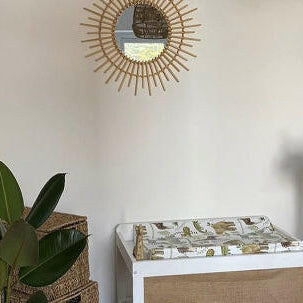Safari wedge changing mat with a green plant and sunburst mirror against a white wall