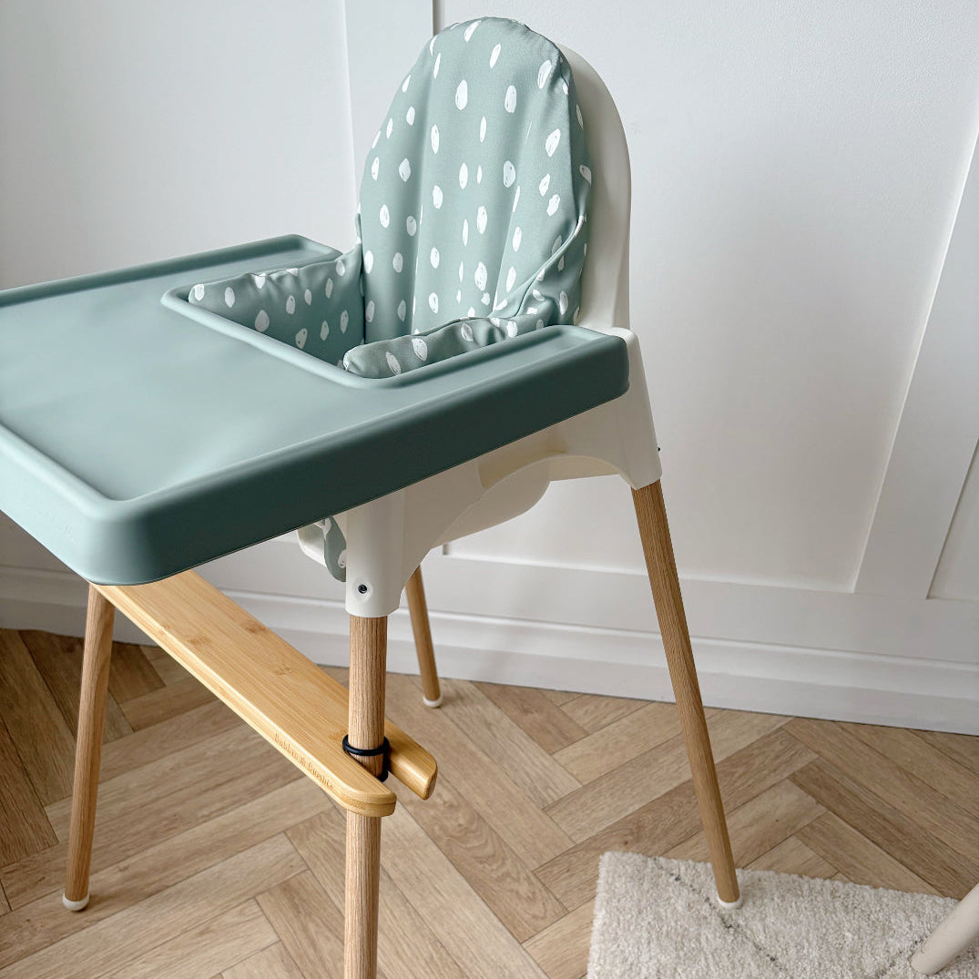 High chair with a green tray and white polka dot cushion on a wooden floor.