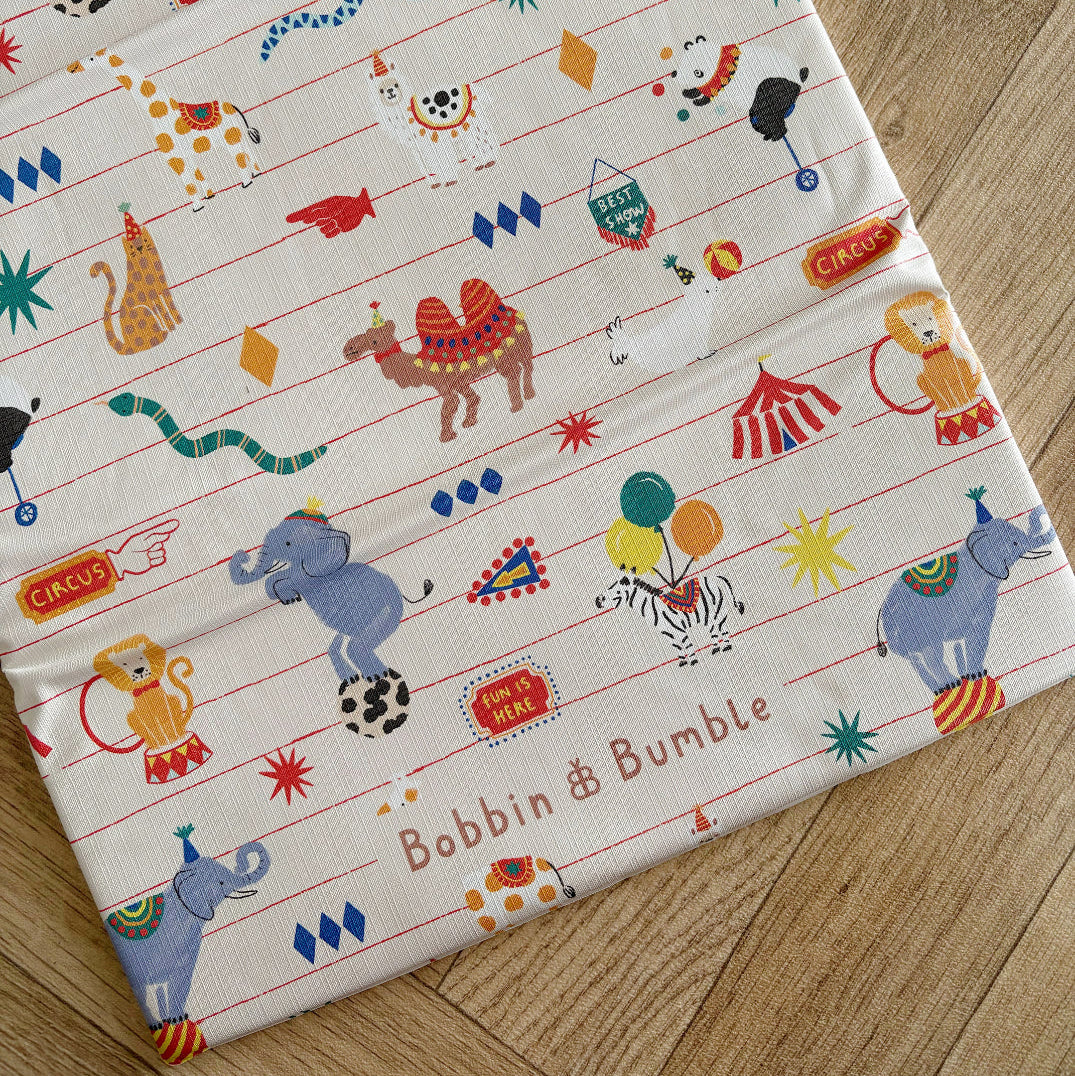 changing mat with circus-themed design featuring animals and Bobbin and Bumble logo, displayed on a wooden surface.