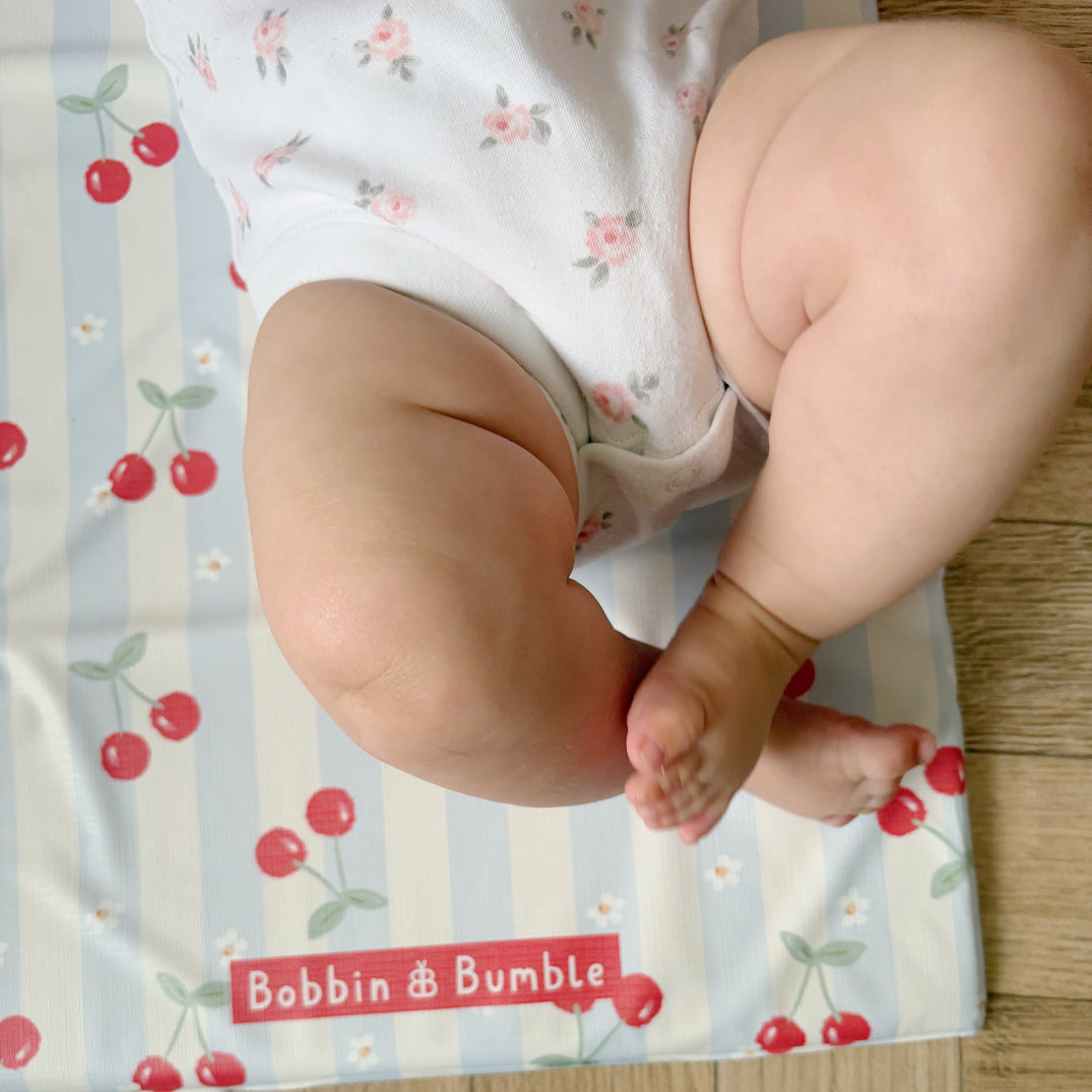 Baby's legs on a cherry-patterned mat with 'Bobbin & Bumble' branding.