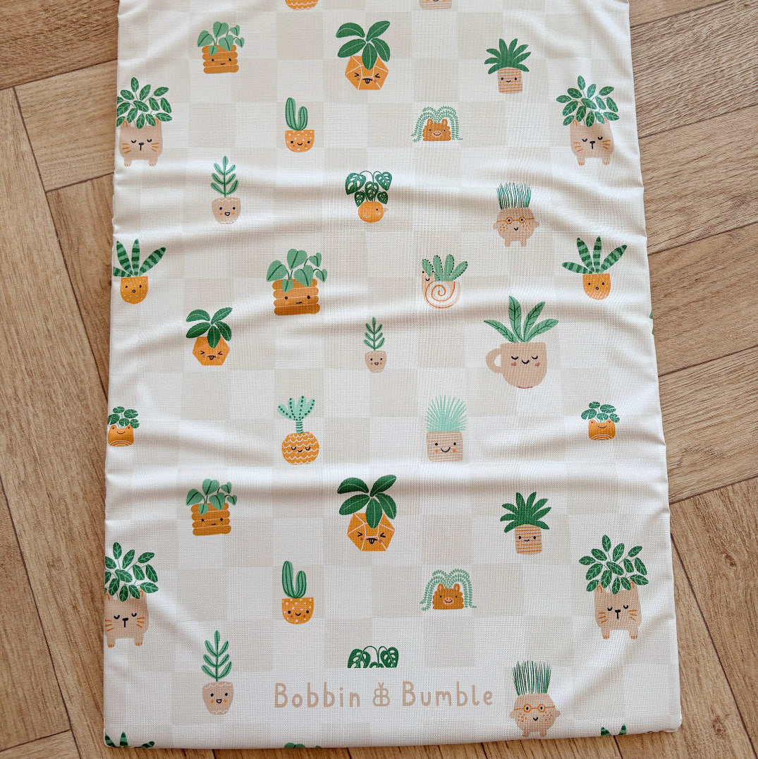 Baby changing mat laid out flat with cartoon plant pattern on wooden floor