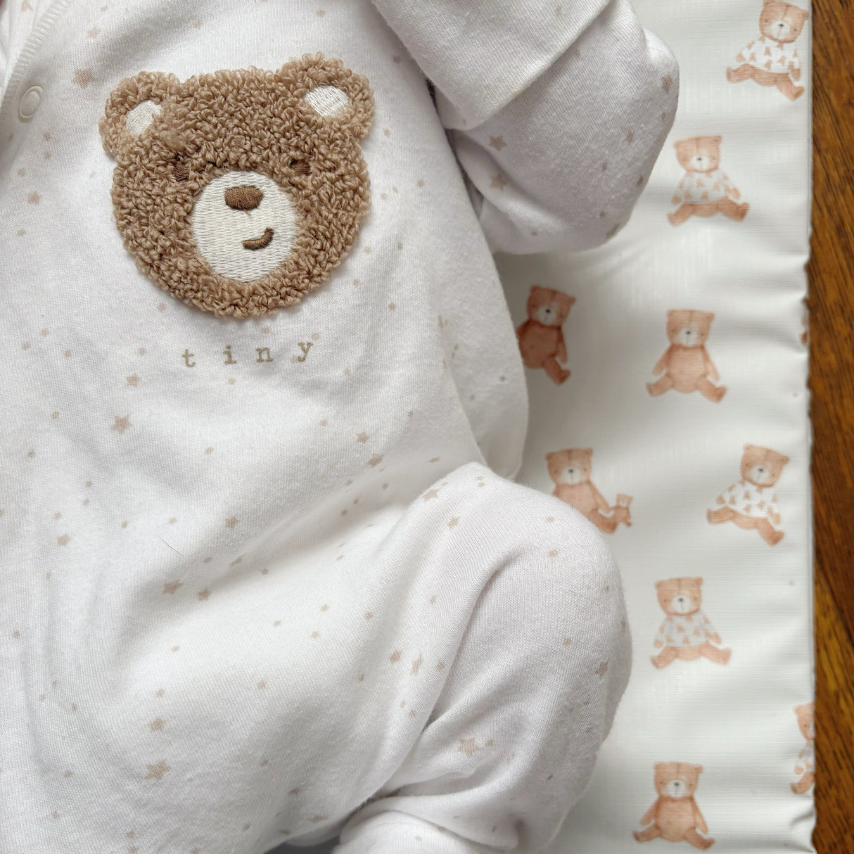 Teddy bear travel changing mat with a baby laying on it in a teddy bear onesie that says tiny.