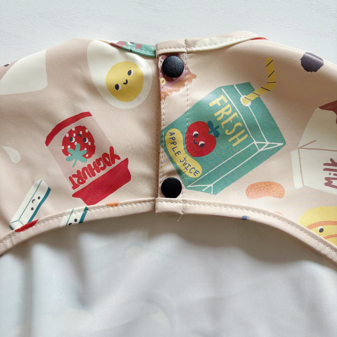 Close-up of a children's bib popper fastening with colourful food-themed illustrations on a light background