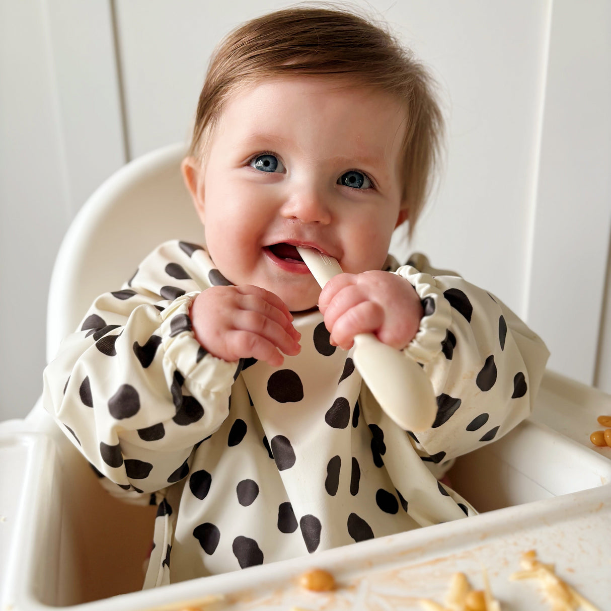 Baby in a highchair smiling wearing a spotty long sleeved bib