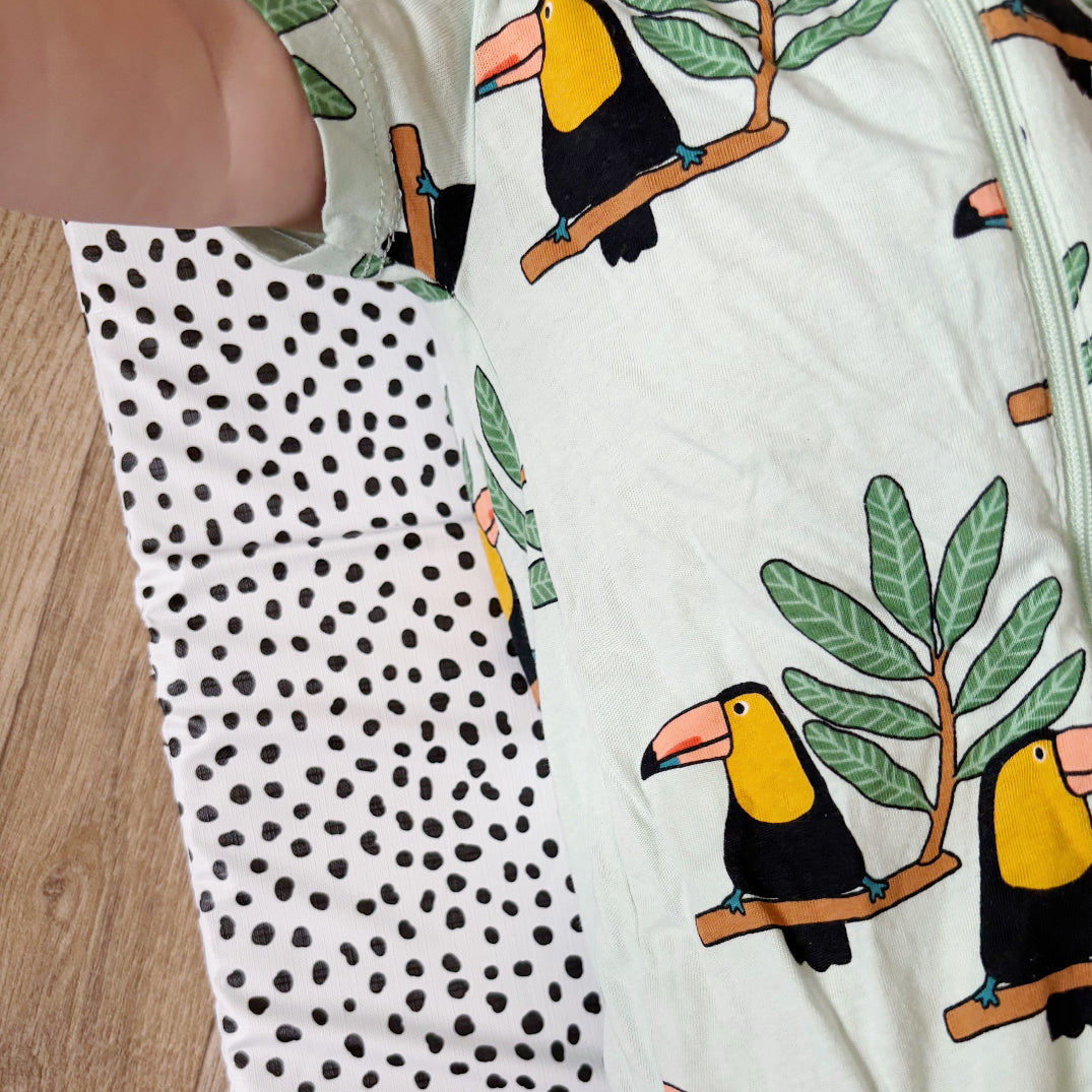 Close-up of a baby onesie with toucan and polka dot pattern changing mat on a wooden floor.