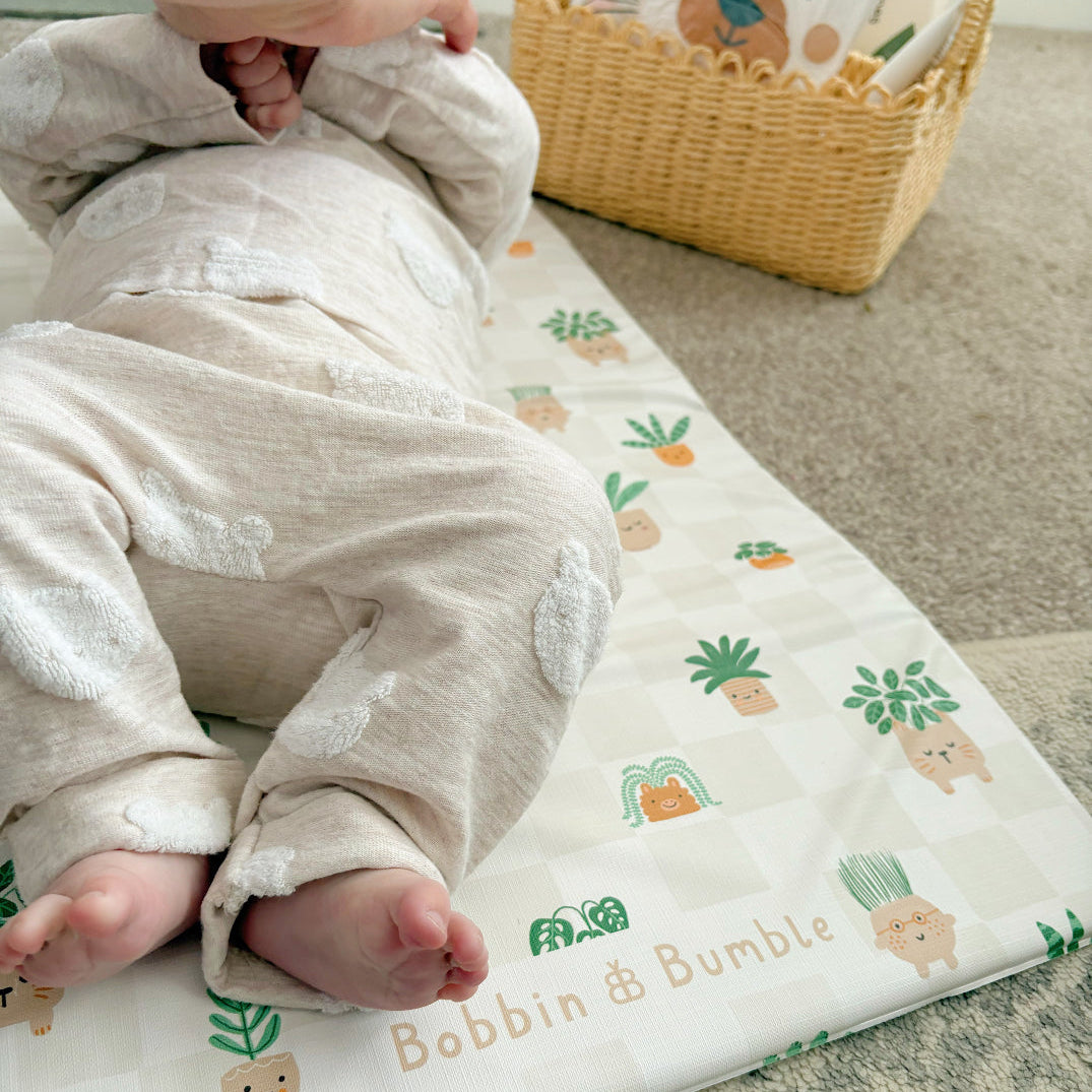 Baby lying on a patterned changing mat with a basket of items in the background.