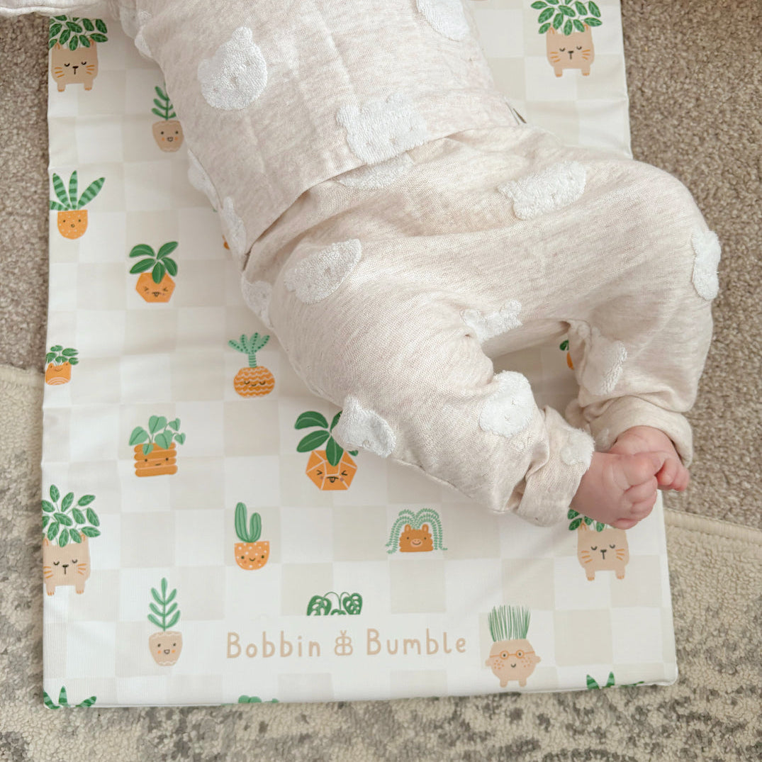 Baby lying on a patterned changing mat with 'Bobbin & Bumble' branding