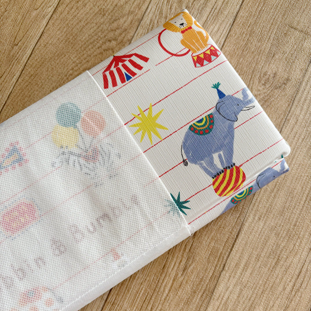Children's folded changing mat with colourful circus pattern on a wooden surface