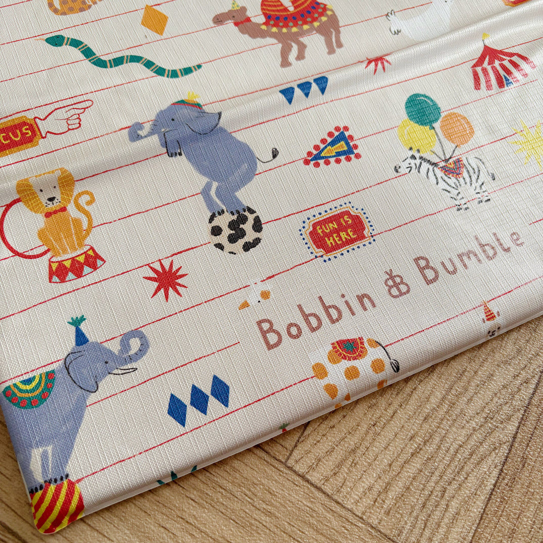 Children's changing mat circus-themed designs and 'Bobbin & Bumble' branding on a wooden surface.