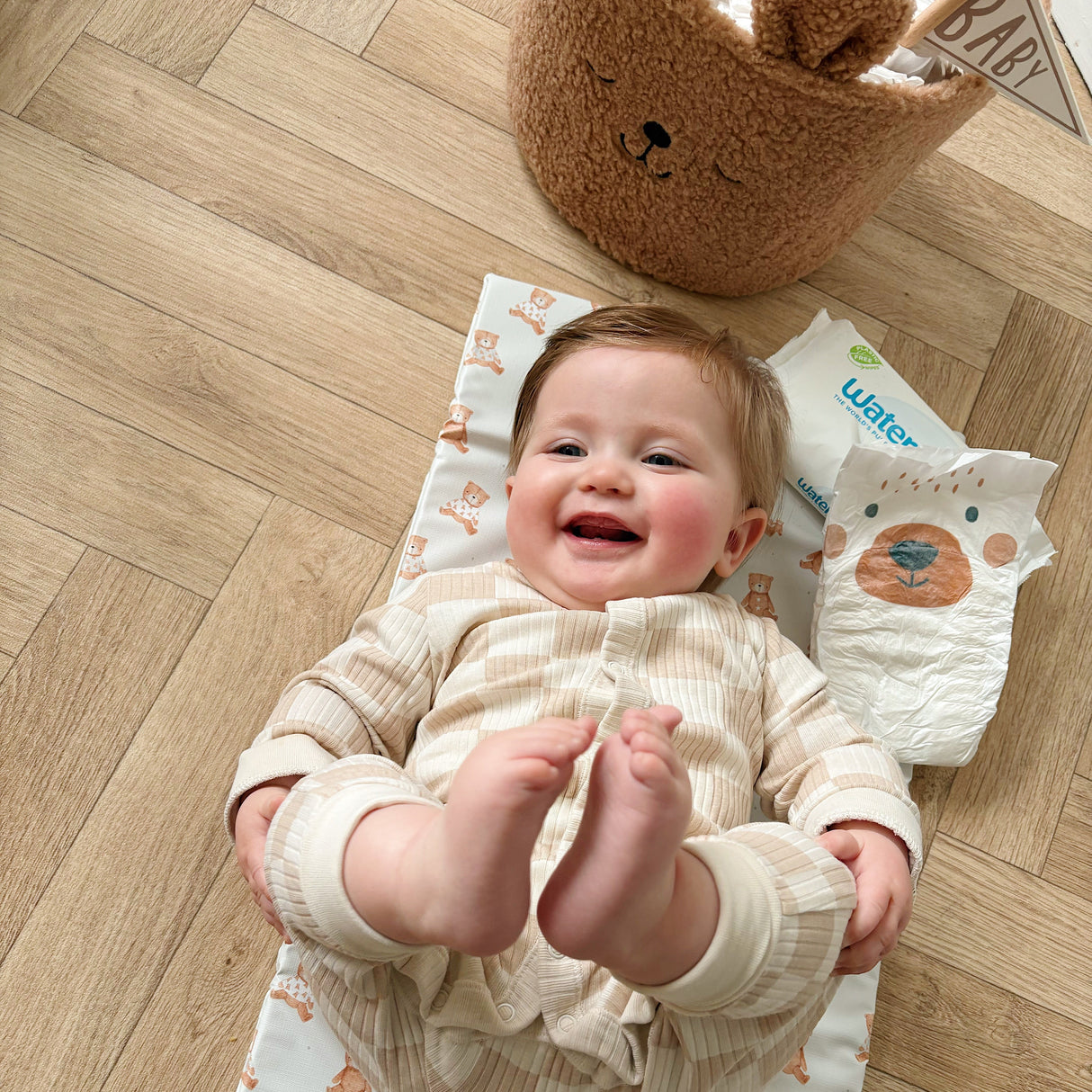 Happy smiling baby laying on a changing mat on the floor with nappy and wipes close by