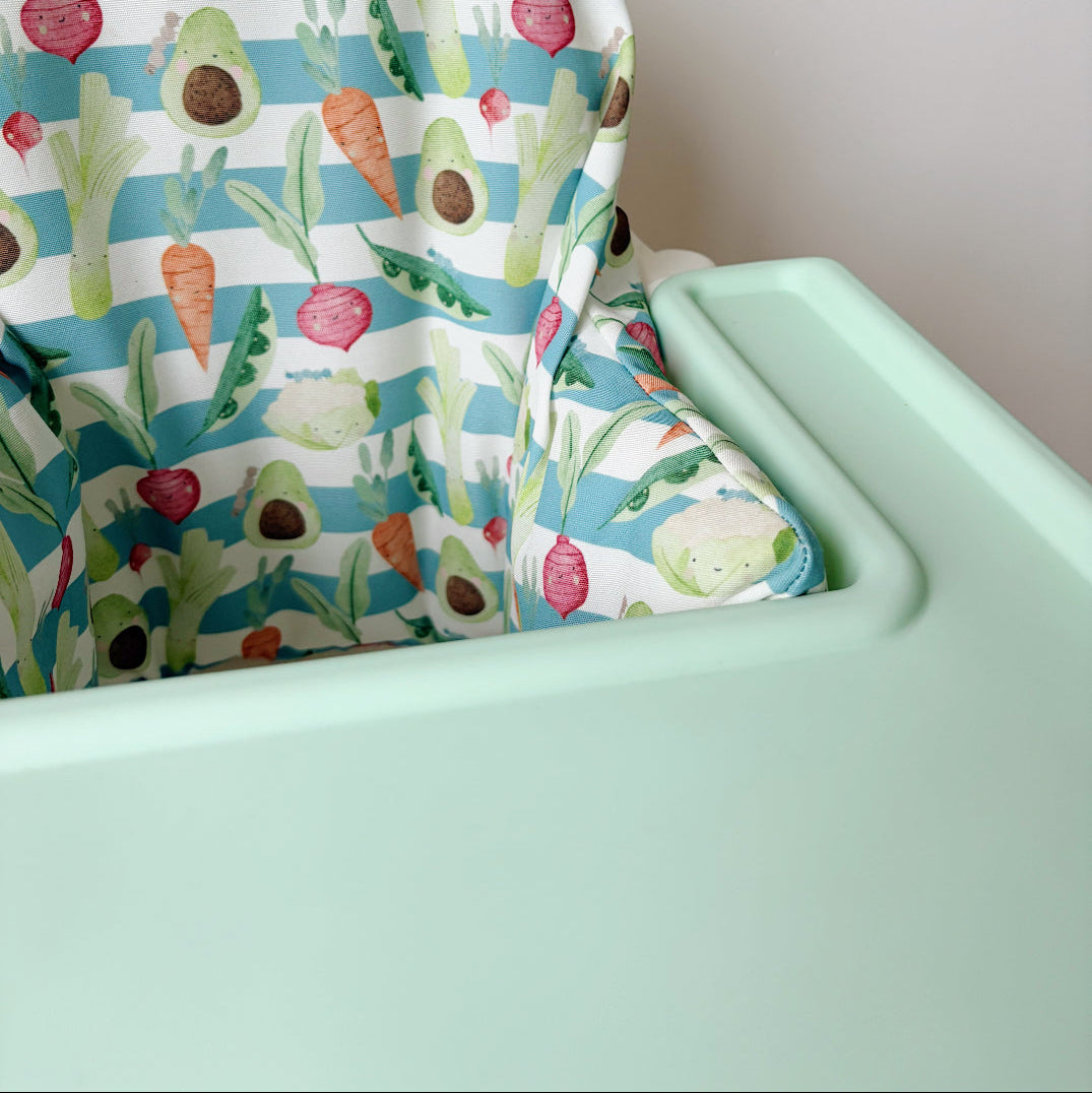 High chair with colorful garden-vegetable patterned cover on a white background
