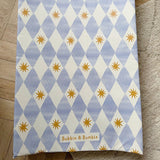 Wedge baby changing mat with blue and white diamond pattern and yellow stars on a wooden floor.