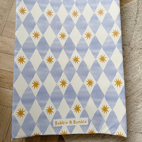 Wedge baby changing mat with blue and white diamond pattern and yellow stars on a wooden floor.