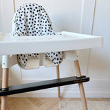 White high chair with black and white polka dot cushion on a wooden floor.