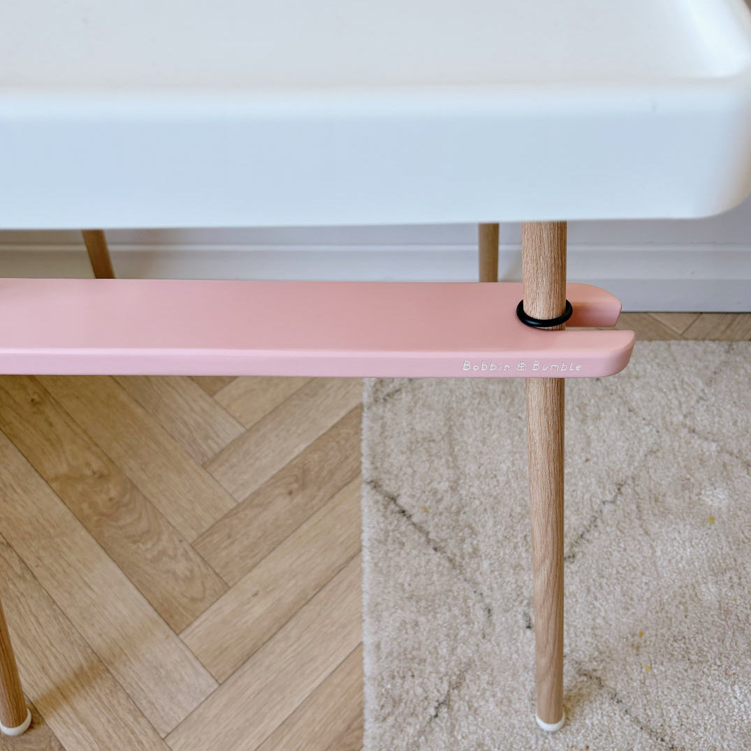 IKEA highchair with Pink footrest with wooden legs on a floor with a white wall in the background