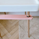 IKEA highchair with Pink footrest with wooden legs on a floor with a white wall in the background