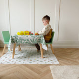 Child sat at a table playing with play-doh. Plant pot splash mat underneath and a leafy green splash mat used as a tablecloth