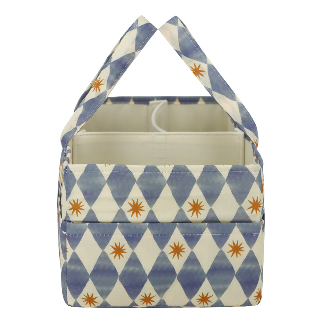 A fabric storage basket with a blue and cream harlequin diamond pattern and small orange starburst accents, featuring two top handles and a cream-colored interior.