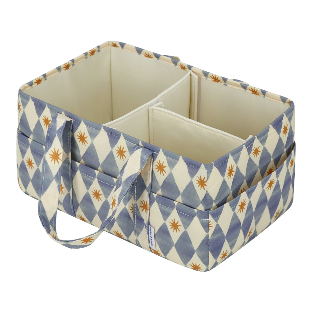A fabric baby storage organizer bin with a blue and cream harlequin diamond pattern accented with small orange starburst motifs. The organizer features multiple compartments, a top handle, and a small fabric brand tag on the front side.