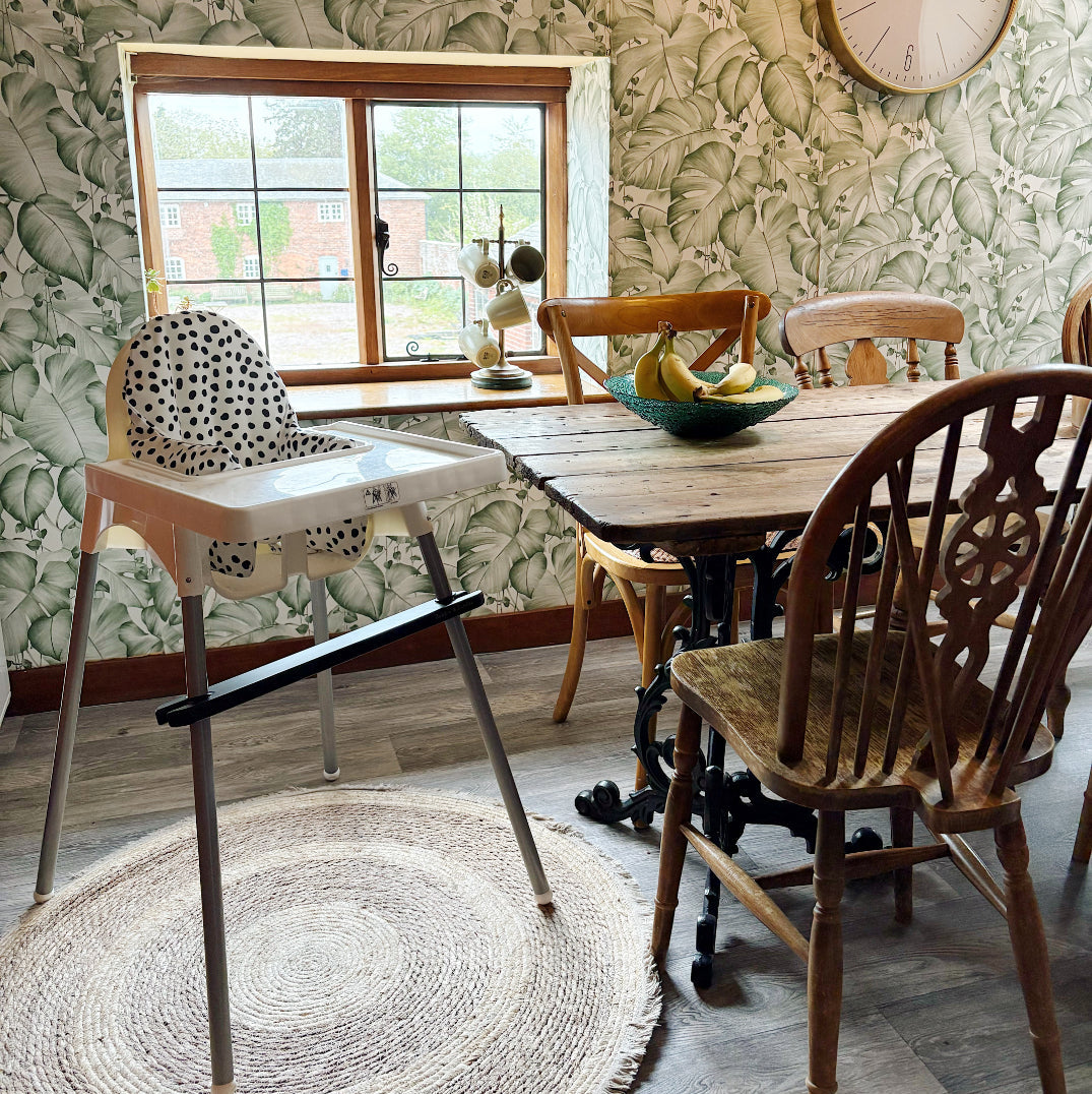 Dining room with wooden table, chairs, and a high chair against a patterned wall.