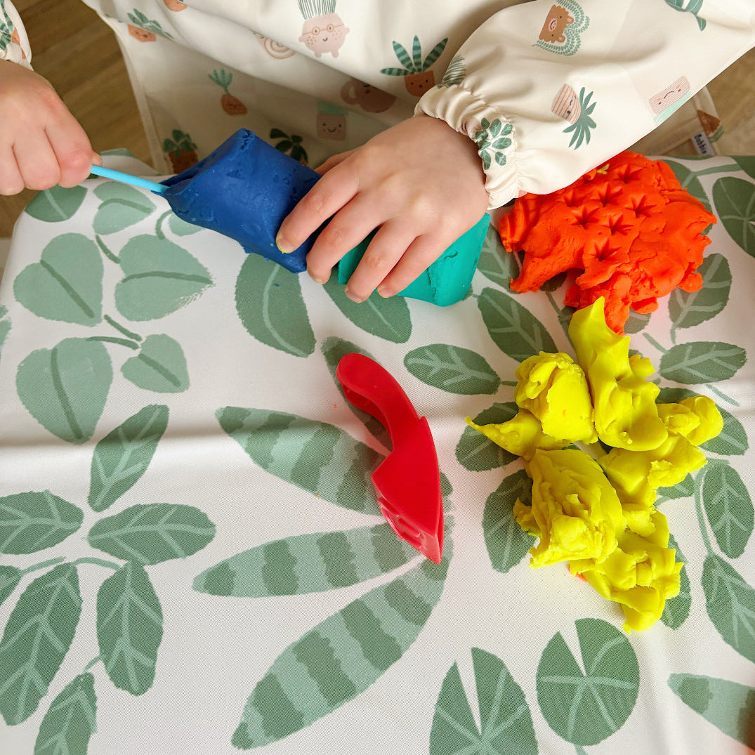 Children's hands playing with colourful Play-Doh on a leaf-patterned splash mat