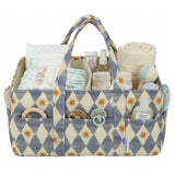 A fabric baby nappy caddy organizer with a blue and cream harlequin pattern and gold starburst motifs, shown filled with baby essentials including nappies, bottles, a rolled towel, a dummy, and teething toys on a white background.