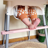 Child's feet on a pink IKEA highchair footrest with 'Bobbin & Bumble' branding, standing on a rug next to a plant.