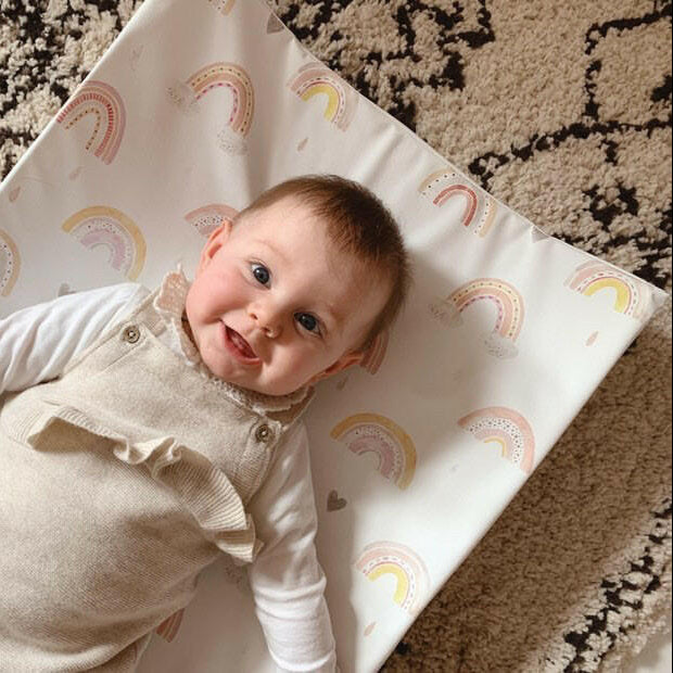 baby smiling on top of a rainbow print changing mat