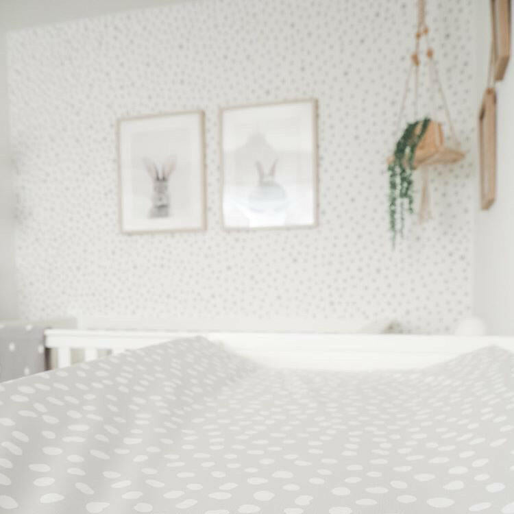 Close up of bobbin and bumble grey wedge shape changing mat. Grey spotty wall and hanging plant in background. 
